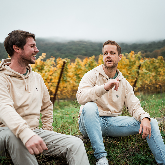 Zwei Pfalz Herz Mitglieder diskutieren sitzend vor Rebenmeer